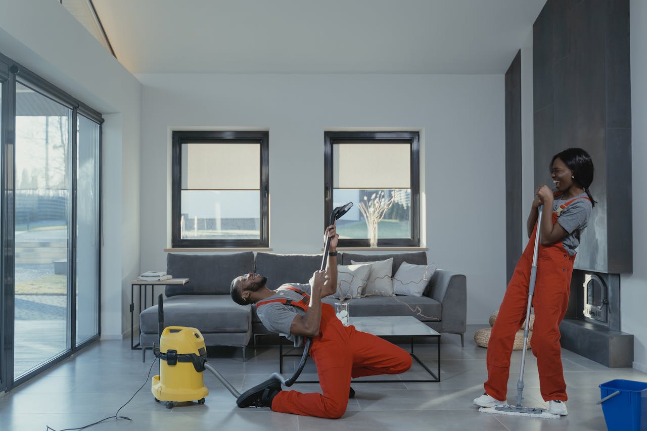 Fun and engaging cleaning session with a man and woman in overalls using cleaning tools in a modern living room.